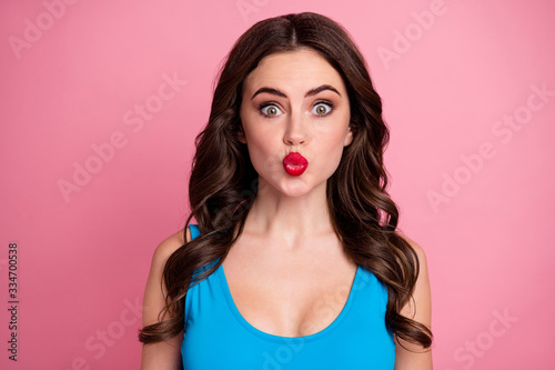 Closeup photo of pretty curly lady sending air kisses boyfriend flirty mood shiny red lipstick tender lips wear casual blue tank-top isolated pink bright color background