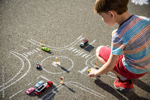 Funny kid boy having fun with picture drawing traffic car with chalks. Creative leisure for children outdoors in summer. Difficult traffic rules concept