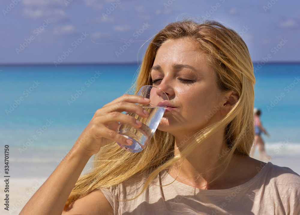Young beautiful girl drinks water on the beach. Woman with a glass of water. Hot beach day. Young beautiful girl drinks water on the beach. Woman with a glass of water. Hot beach day.