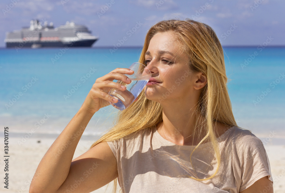 Young beautiful girl drinks water on the beach. Woman with a glass of water. Hot beach day. Young beautiful girl drinks water on the beach. Woman with a glass of water. Hot beach day.