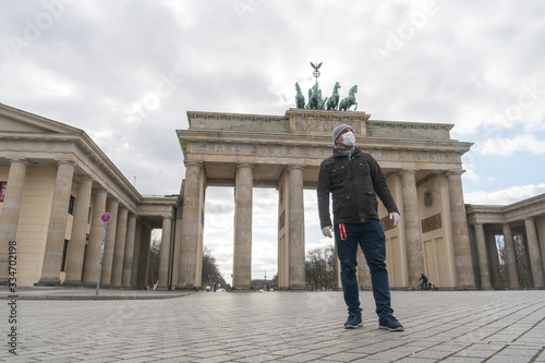 Tourist wearing medical protective mask and gloves posing alone in front of the Brandenburg Gate during the city's lockdown