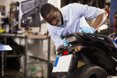 Afro american worker inspects the wheel of a motorcycle © JackF