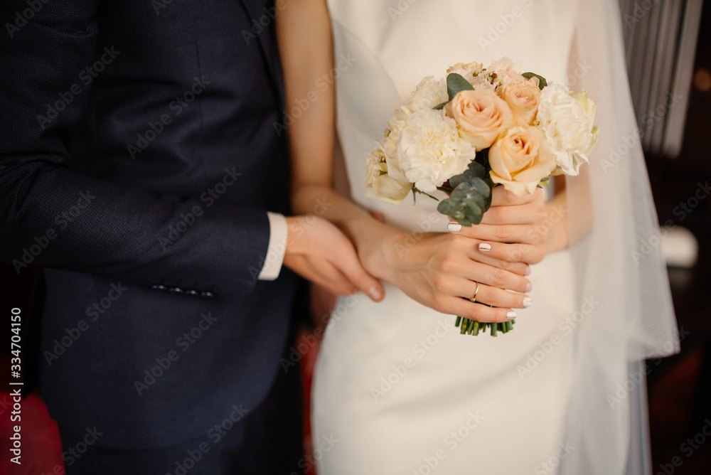 The groom holds the bride by the hand, the bride holds a bouquet, close-up. Wedding details. The groom holds the bride by the hand, the bride holds a bouquet, close-up. Wedding details.