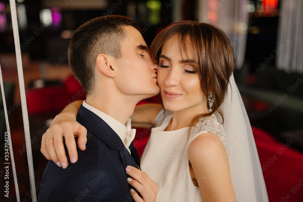 Groom kisses the bride on the cheek, close-up. Newlyweds in a modern interior. Wedding, love, relationship concept. Groom kisses the bride on the cheek, close-up. Newlyweds in a modern interior. Wedding, love, relationship concept.