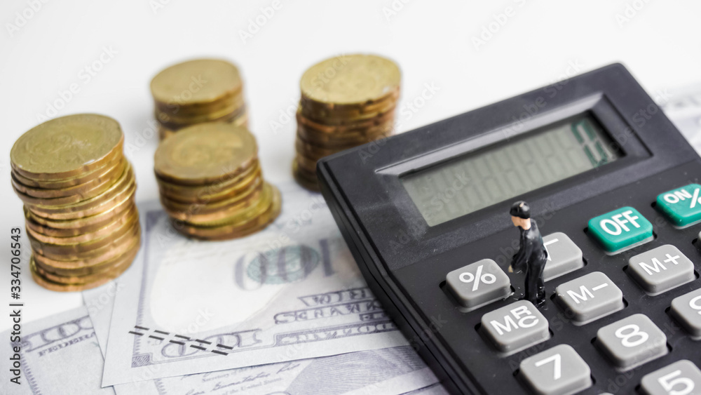 Selective focus on figurine of businessman on calculator with money and coins in background. Tax savings concept. Selective focus on figurine of businessman on calculator with money and coins in background. Tax savings concept.