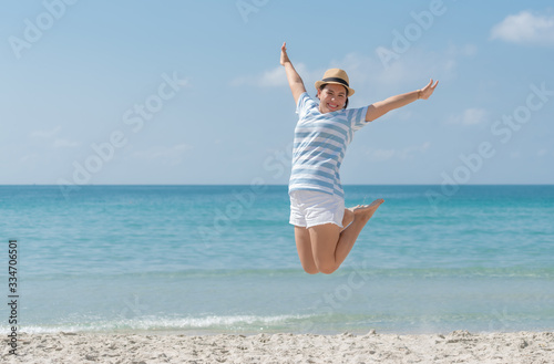 Asian young woman wearing a hat is jumping with enjoy and happiness on the beach.