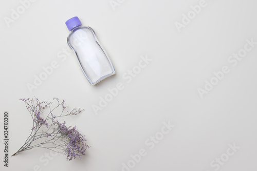 purple cosmetic bottle and flower on light yellow background with copy space