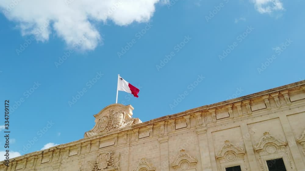Maltese flag on Castille Palace in Valletta city - capital of Malta island. Blue sky and clouds