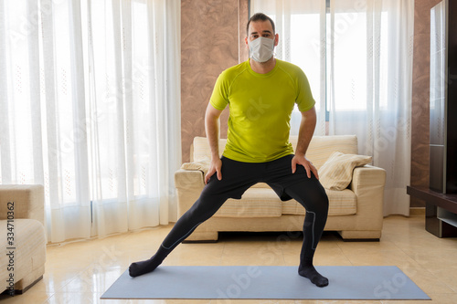Low-bearded man exercising with black and green sportswear and mask to prevent coronavirus