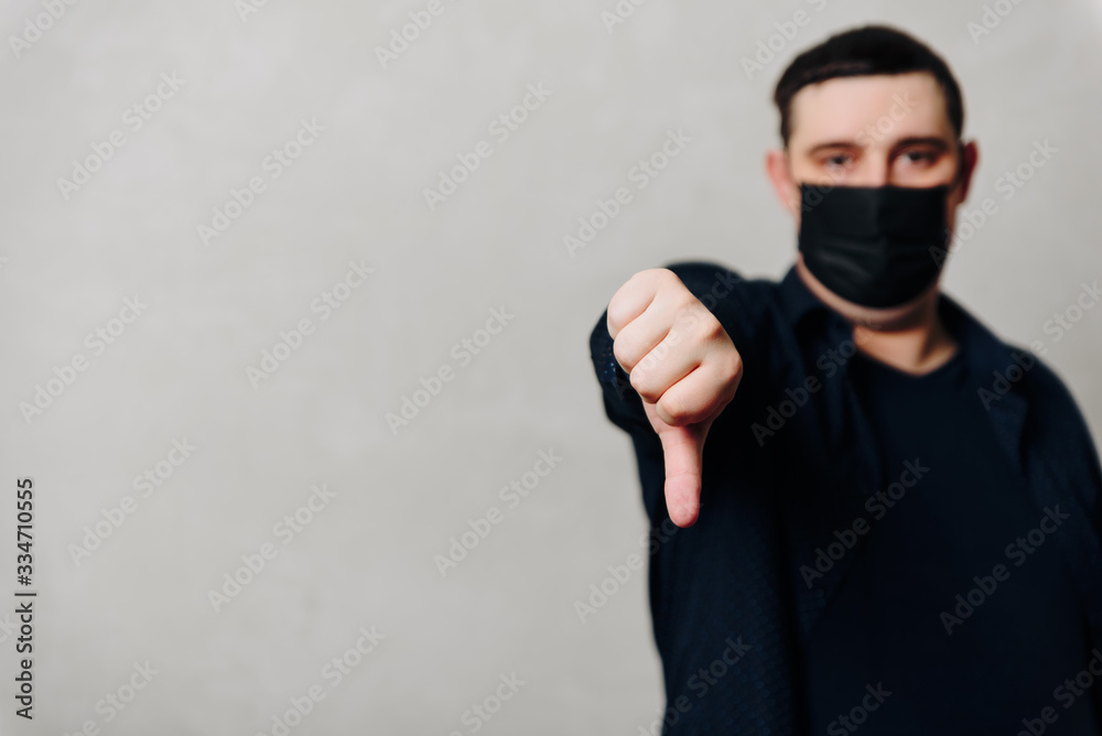 a man in a black medical mask on a gray background gives a thumbs down a man in a black medical mask on a gray background gives a thumbs down