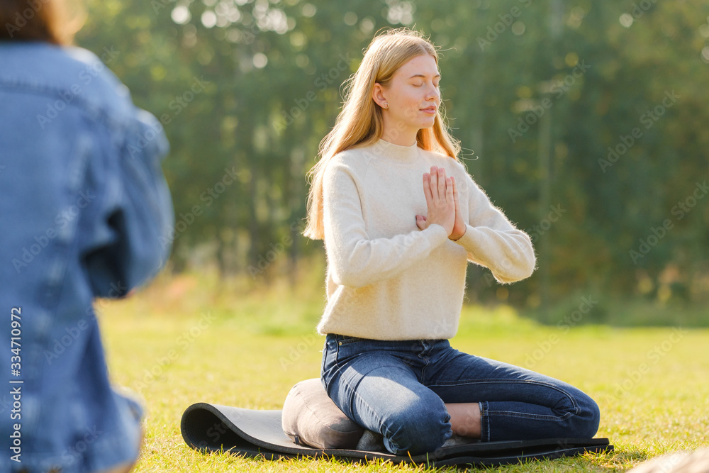 A group of young people meditate outdoors in a park. 