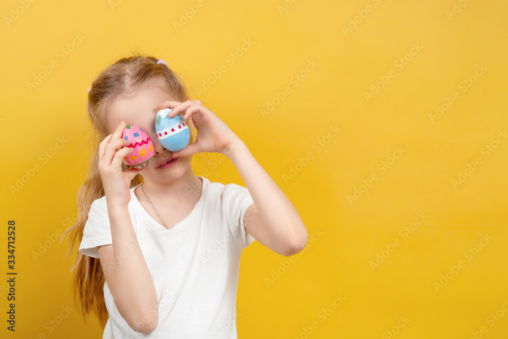 Cute girl in t shirt smiling and keeping colored eggs near eyes while having fun during Easter celebration against yellow background Cute girl in t shirt smiling and keeping colored eggs near eyes while having fun during Easter celebration against yellow background