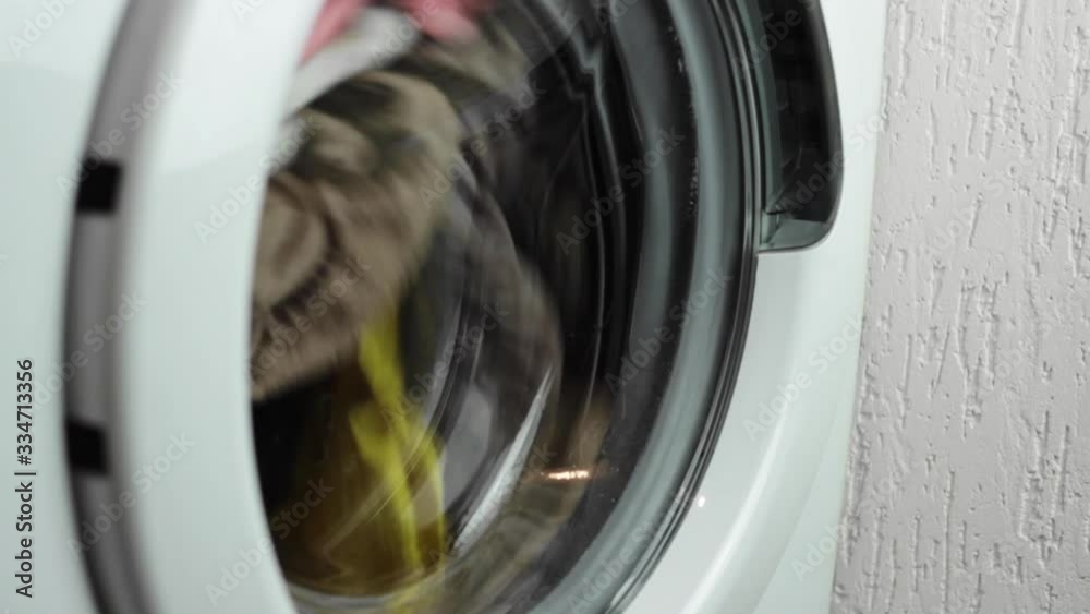 Rising view of a washing machine spinning a load of mixed colours clothes and then stopping