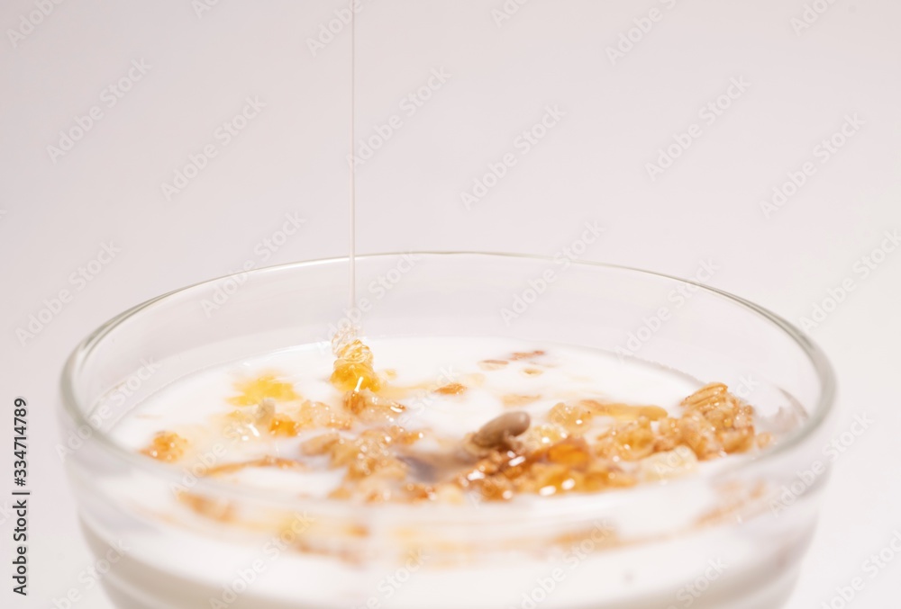 A stream of honey pours on the musli with milk in a transparent glass. Breakfast containing vitamins and minerals A stream of honey pours on the musli with milk in a transparent glass. Breakfast containing vitamins and minerals