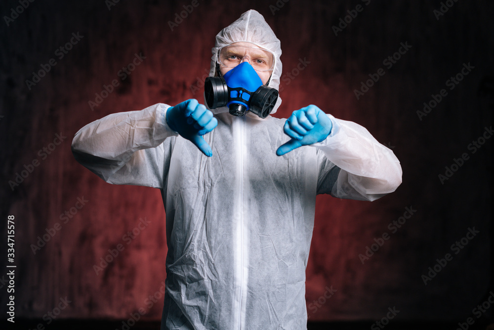 Serious man medical doctor wearing protective suit, goggles and respirator is showing thumbs down gesture. Concept of Coronavirus COVID-19 Pandemic. Studio shot on isolated dark red background. Serious man medical doctor wearing protective suit, goggles and respirator is showing thumbs down gesture. Concept of Coronavirus COVID-19 Pandemic. Studio shot on isolated dark red background.