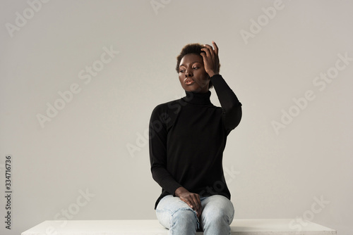 Canvas Print tender african american girl in jeans and black turtleneck sitting on white cube