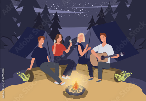 Group of friends camping. They are sitting around camp fire and playing guitar