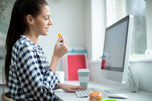 Fotografie, Obraz Female Worker In Office Having Healthy Snack Of Dried Apricot Fruit