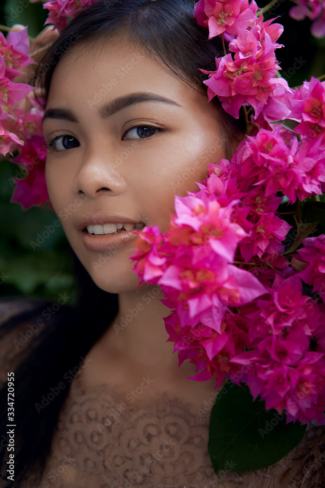 Asian girl portrait face in pink flowers. Beautiful Balinese women. Beauty salon and massage spa concept Asian girl portrait face in pink flowers. Beautiful Balinese women. Beauty salon and massage spa concept