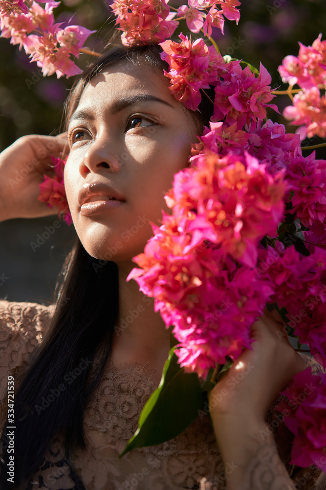 Naklejka premium Asian girl portrait face in pink flowers. Beautiful Balinese women. Beauty salon and massage spa concept