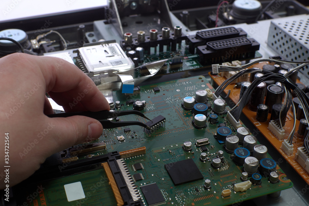 Man's hand holds a chip with tweezers. Electronics repair. Disassembled LCD TV. Radio electronic components. Circuit Board LCD TV. Master electronic engineer. Man's hand holds a chip with tweezers. Electronics repair. Disassembled LCD TV. Radio electronic components. Circuit Board LCD TV. Master electronic engineer.