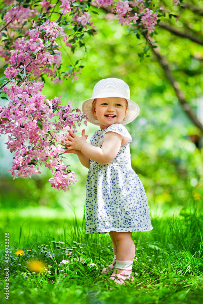 Close-up portrait of a 1-2 year old girl outdoors in a garden with pink flowers in the trees. Close-up portrait of a 1-2 year old girl outdoors in a garden with pink flowers in the trees.