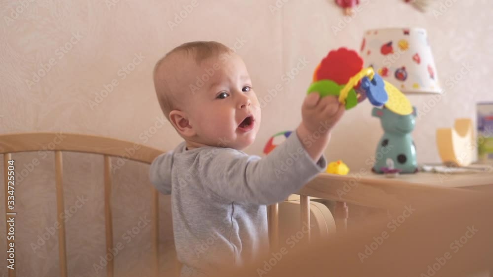 Kid Playing in Crib. Nine Month Old Baby Stands in Crib and Plays with Toy. Child Throws Toy in Slow Motion Kid Playing in Crib. Nine Month Old Baby Stands in Crib and Plays with Toy. Child Throws Toy in Slow Motion