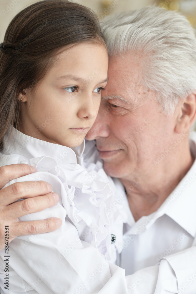 Portrait of sad grandfather and granddaughter hugging at home Portrait of sad grandfather and granddaughter hugging at home