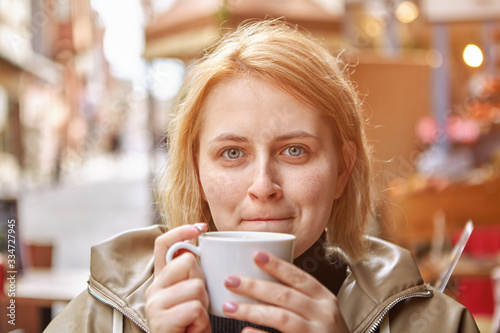 White female tourist drinks coffee in street cafe.