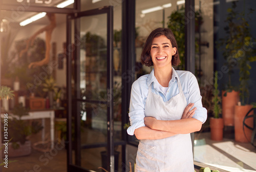 Obraz na płótnie Portrait Of Smiling Female Owner Of Florists Standing In Doorway Surrounded By P