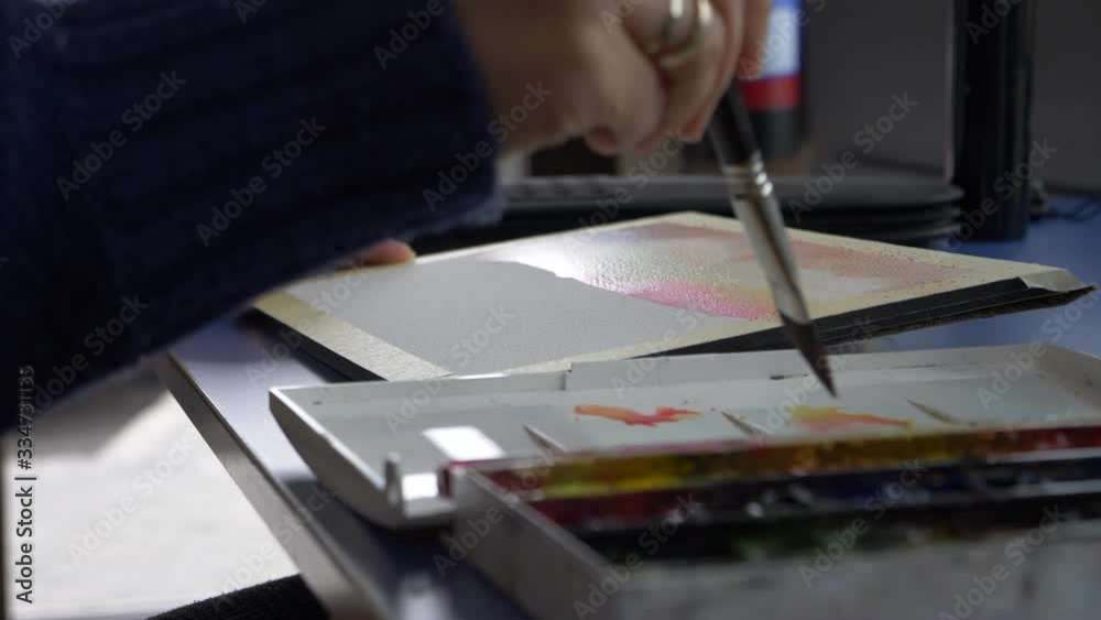 woman's hand painting and dipping the brush in a watercolor color palette woman's hand painting and dipping the brush in a watercolor color palette
