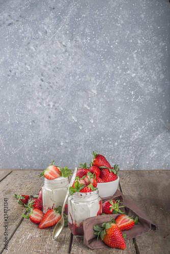 Sweet healthy yogurt with strawberry and strawberry jam in small portioned jars on wooden rustic table, copy space