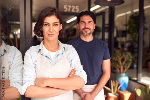 Portrait Of Male And Female Owners Of Florists Standing In Doorway Surrounded By Plants