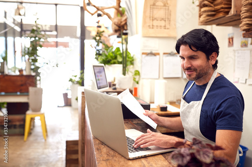 Fotografie Male Sales Assistant Working On Laptop Behind Sales Desk Of Florists Store