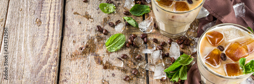 Cold summer coffee, latte, frappe, frappuccino. Coffee iced cocktail drink with frozen coffee ice cubes, milk or non-dairy milk and mint leaves. Wooden background copy space