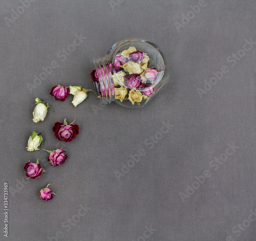 Fototapeta Naklejka Na Ścianę i Meble -  Dried rose heads with glass jar on grey cloth background. Pink and white rose buds. Copy space, top view