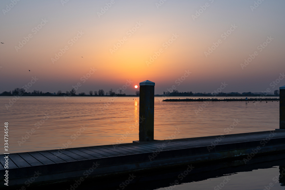 The setting sun almost disappears behind one of the bollards of a landing stage at Lake Zoetermeerse Plas in Zoetermeer, The Netherlands
