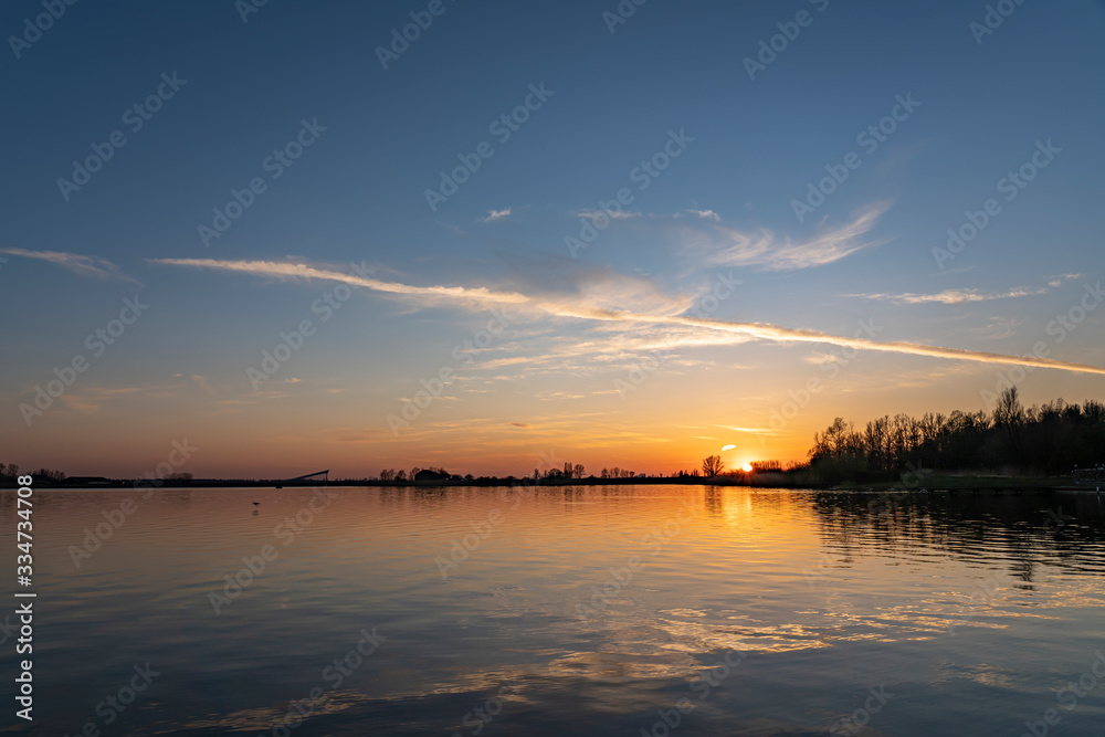 A single contrail over lake Zoetermeerse Plas is illuminated during sunset in Zoetermeer, Netherlands