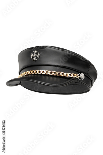 Subject shot of a black leather peak cap with a golden chain under the visor and a metal stylized cross on the crown. The stylish headwear is isolated on the white background.