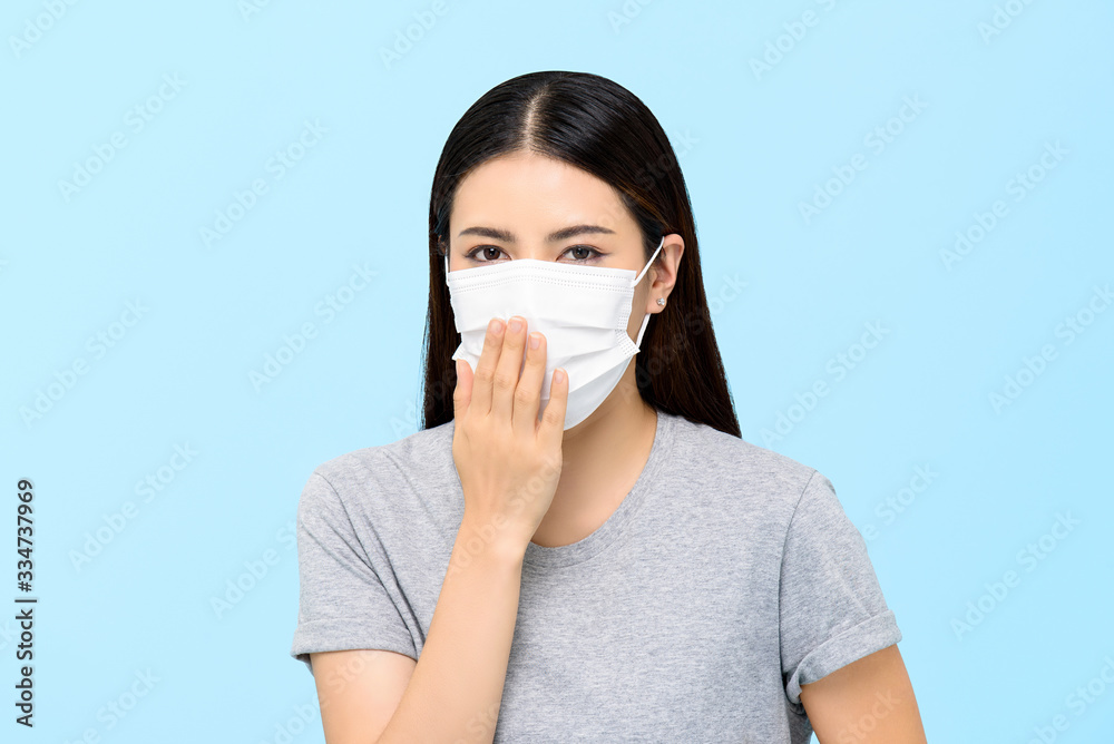 Asian woman wearing medical face mask coughing isolated on light blue background Asian woman wearing medical face mask coughing isolated on light blue background