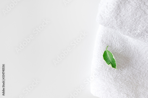 Clean bath towel and fresh green leaf on white background with copy space and selective focus. Concept health care spa and hygiene. Domestic bathroom, indoors
