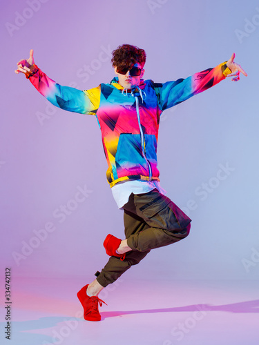 Guy dancing contemporary dance in studio. Neon light grey background. Acrobatic bboy dancer. Break dance lessons.