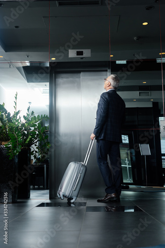 Back view of businessman with travel bag standing near elevator