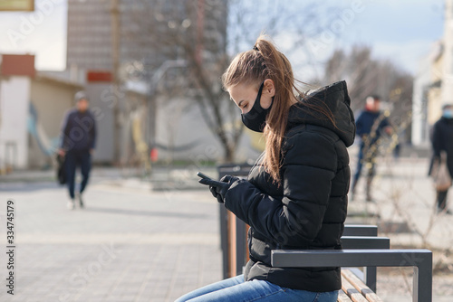 Young woman sitting on a street bench with medical mask and black clothes