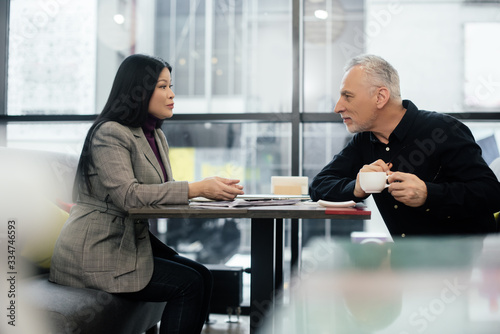 side view of businessman and asian businesswoman talking in cafe