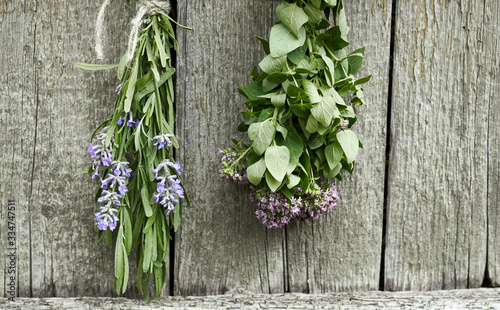 Lavender and oregano tufts hanging under the roof and drying on the background of old textured wooden wall, closeup, copy space, agriculture and aroma herbs concept