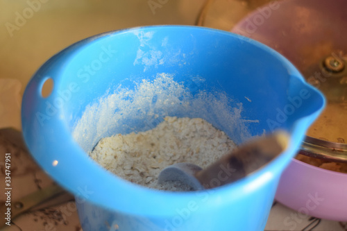 Blue bowl with flour and wooden spoon on the table in the kitchen close up