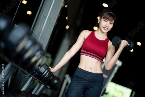 Young healthy asian woman lifting dumbbells in the gym. Exercise, workout, muscle training, weight lifting, weight loss, heart rate practice and diet concept.