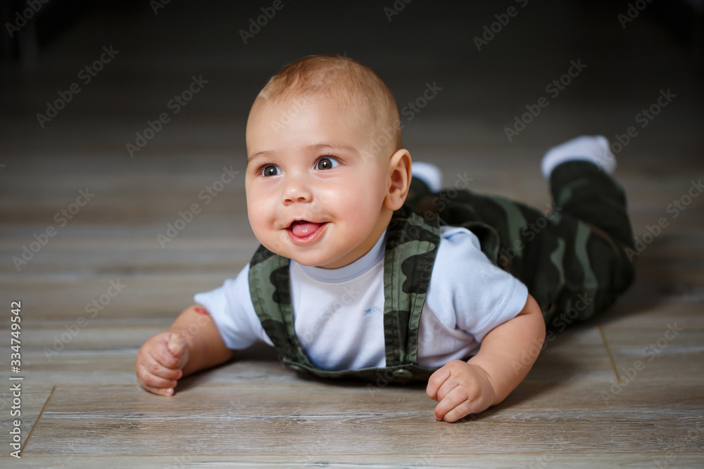 Naklejka premium little boy aged 8 months in overalls, a white shirt and white socks crawling on the floor and smiling
