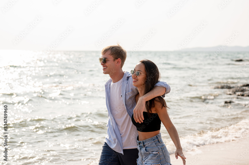 Couple caucasian and latin are walk together at the beach with sunset. Summer vacation relaxation, travel, nature, happy life unseen concept.